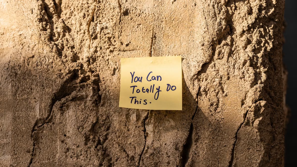 A sticky note with a motivational message on a textured wall in Dubai, with sunlight casting shadows.